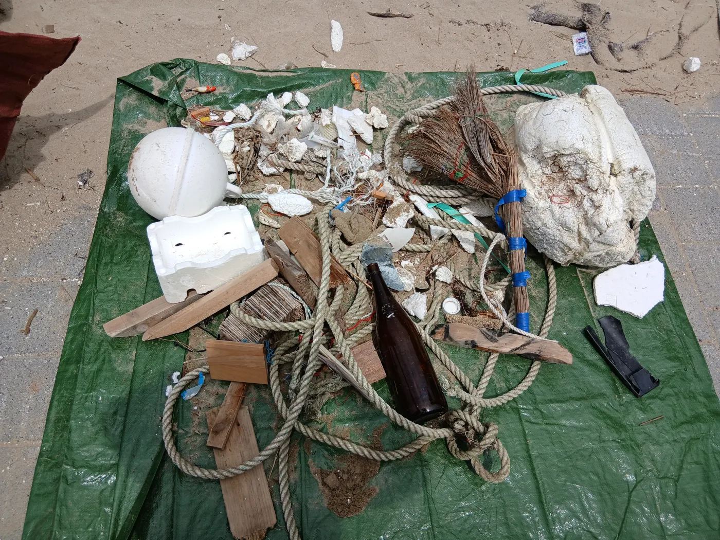 수거한 쓰레기를 초록색 방수포 위에 펼쳐 놓은 사진. 스티로폼 부표와 조각, 밧줄, 나무 조각, 유리병이 겹치지 않게 놓여 있다.